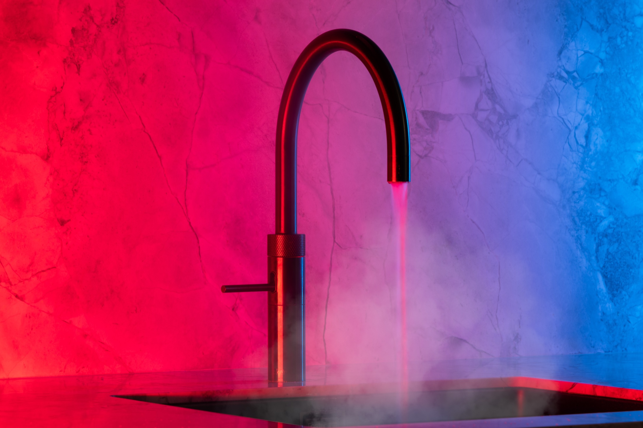 Rubinetto con acqua e vapore, illuminato da luce rossa e blu